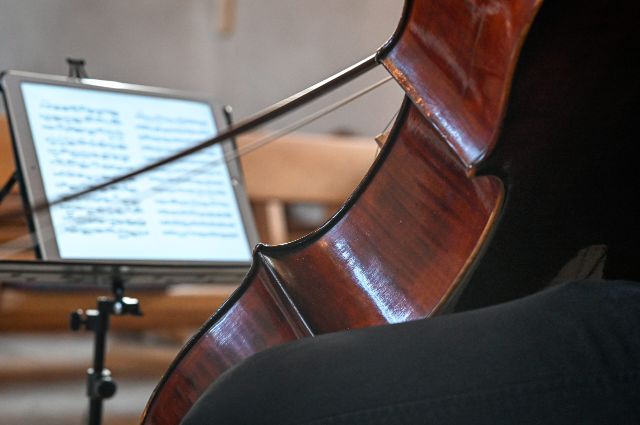 Die Rückseite eines Cellos, ein Bogen und ein unscharfes Notenblatt im Hintergrund
