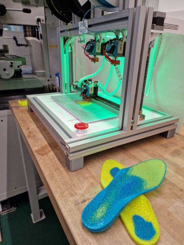 Der 3D-Drucker bei der Arbeit. Grüne LEDs beleuchten den gelben Kunststoff, mit dem Gedruckt wird.